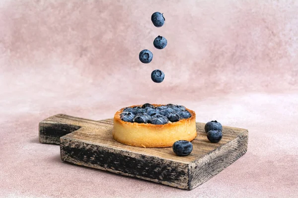 Surreal design with floating berry. Blueberry pie on a wooden board. Blueberry tart. Creative fly food concept.