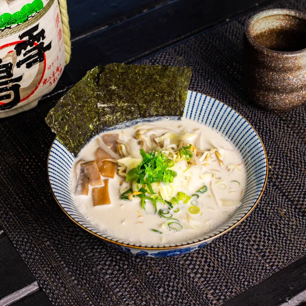 Soy milk white soup veggie ramen in the traditional Japanese ramen restaurant, with a ramen bowl on a black mat and Japanese fonts sake barrel translation: Snow Crane