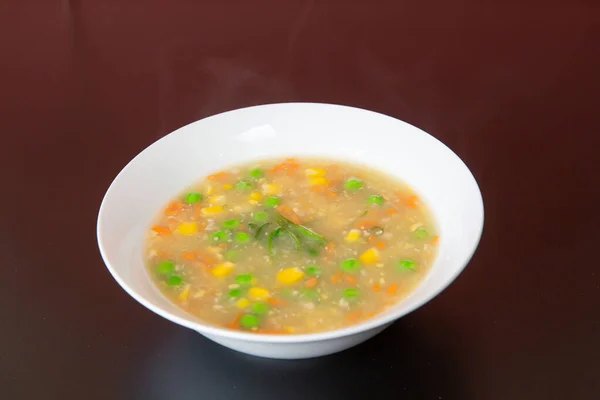 Chicken and cream corn chowder soup of traditional Cantonese yum-cha Asian gourmet cuisine meal food dish on the white serving plate and brown red table