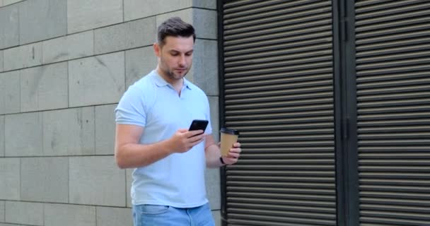 Primer plano sonriente hombre con café hablando de teléfono móvil cerca de la oficina. hermoso día — Vídeos de Stock