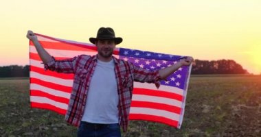 Ekose gömlekli Amerikalı bir adam, tarlada Amerikan bayrağıyla yürüyor..