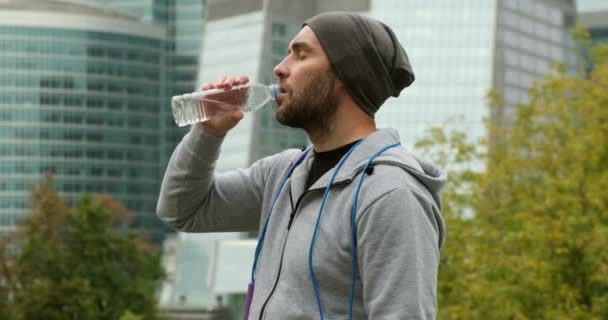 Retrato del hombre activo bebiendo de la botella de agua mientras descansa del entrenamiento — Vídeos de Stock