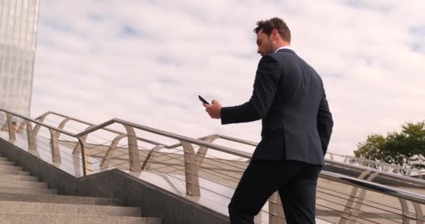 Hezký podnikatel procházení jeho Smartphone v blízkosti moderní kancelářské budovy — Stock video