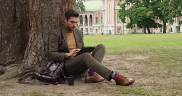 Веселый многонациональный бизнесмен, работающий рядом с деревом, улыбаясь электронным планшетом — стоковое видео