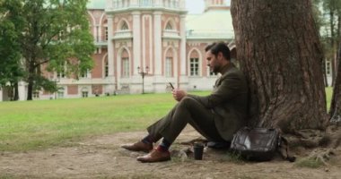 Parktaki bir ağacın yanında oturan yakışıklı işadamı Viyana Avusturya 'da telefon kullanıyor.
