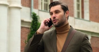 Eski caddede telefonunu kullanarak yürüyen yakışıklı bir iş adamı. Londra