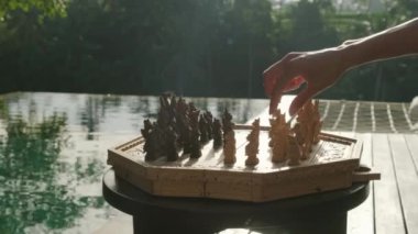 Bir erkeğin eli, havuz kenarında el yapımı bir satrançta kraliçeden bir parça alır.