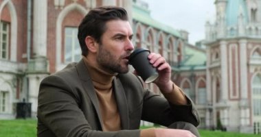 Şehir parkında öğle yemeğinde kahve içen adam sessizliğin tadını çıkar.