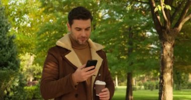 Parkta kahve içip telefonda konuşan bir adam.