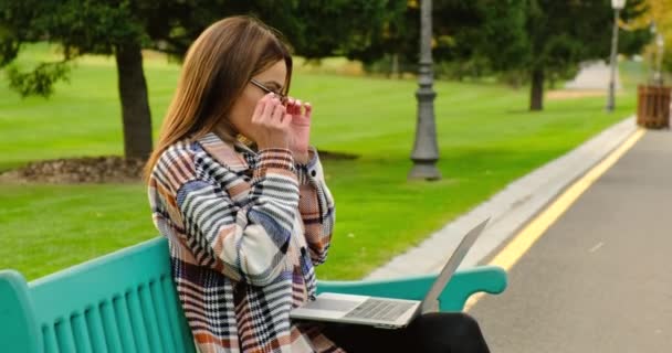 Retrato de hombre de negocios con anteojos sentado con café y portátil en el parque — Vídeos de Stock