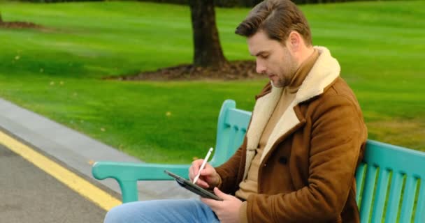 Zakenman met behulp van tablet computer in het park op bank op pauze van het werk — Stockvideo