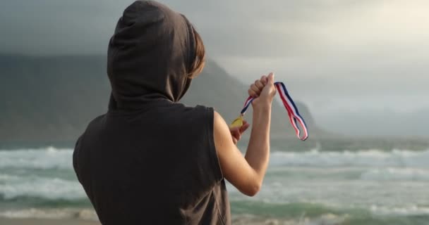 Chica deportiva en la playa cerca del océano levanta victoriosamente una medalla de campeones — Vídeos de Stock
