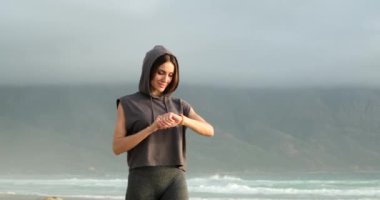 Okyanus kıyısındaki plajda spor yapan kız spor takip cihazını kontrol ediyor. akıllı saat
