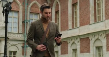 Kahverengi takım elbiseli başarılı bir işadamı telefon ve kahve ile işe gider.