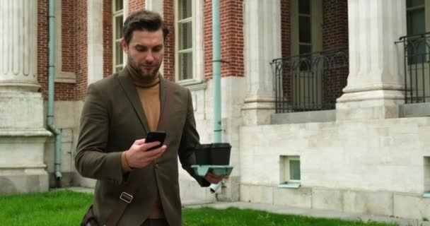 Успешный бизнесмен в коричневом костюме с телефоном и кофе идет на работу — стоковое видео