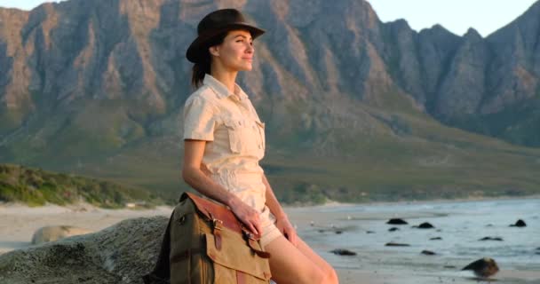 Girl backpacker traveler enjoys with fresh ocean wind. traveler sits on a stone — Stockvideo