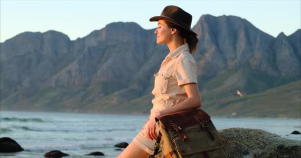 Κορίτσι ταξιδιώτη backpacker απολαμβάνει με φρέσκο αέρα του ωκεανού. Ταξιδιώτης κάθεται σε μια πέτρα — Αρχείο Βίντεο