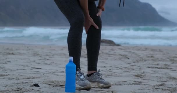 Sección baja de la atleta que sufre de dolor de rodilla en la playa durante el día soleado — Vídeos de Stock