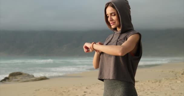 Woman checking data on fitness tracker after training outdoors near ocean beach — Stock Video