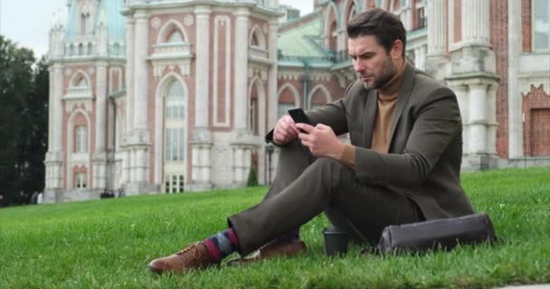 Student in suit and turtleneck sitting on the grass on the university campus — Stock Video