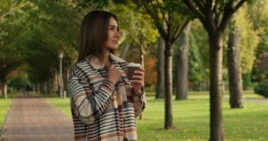Uzun saçlı, ekose ceketli bir kız Sonbahar sıcacık parkında çay ya da kahve içer