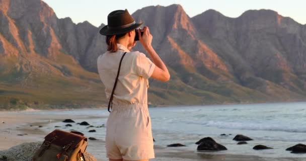 En flicka i en safari hatt gör ett foto vid havet solnedgången Kapstaden — Stockvideo