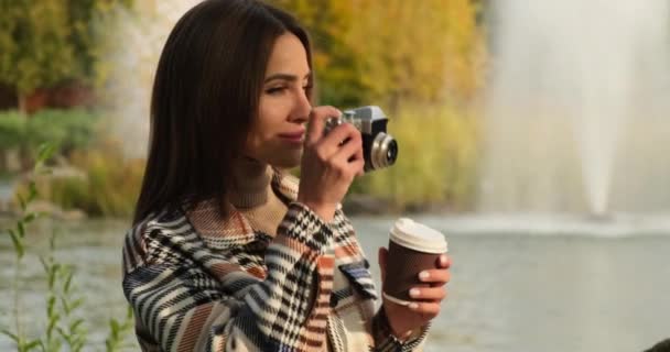 Lány egy kockás kabát iszik teát vagy kávét egy őszi meleg park szökőkút, madarak — Stock videók