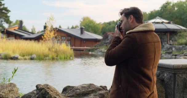 Man reiziger in een trench jas maakt een foto op een film camera in de buurt van de fontein — Stockvideo