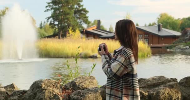 Menina viajante em um casaco de trincheira faz uma foto em uma câmera de filme perto da fonte — Vídeo de Stock