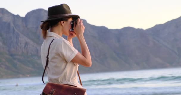 Tourist with backpack in african safari style near the ocean beach takes a photo — Vídeo de Stock