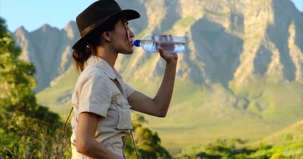 Meisje reiziger drinkt water in de bergen bij zonsondergang in safari kleding — Stockvideo