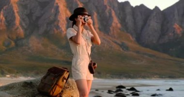 Sırt çantalı turist, Afrika safarisi tarzında, okyanus kıyısında fotoğraf çekiyor.