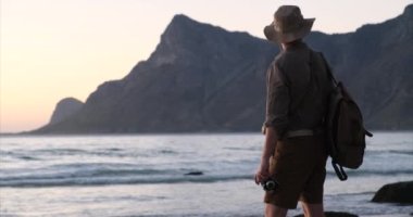 Sırt çantalı turist, Afrika safarisi tarzında, okyanus kıyısında fotoğraf çekiyor.