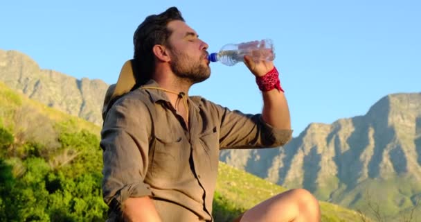 Ember utazó iszik vizet a hegyekben naplementekor szafari ruhákban — Stock videók