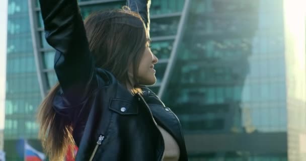 Girl on the background of skyscrapers happily spreads hands and shows thumbs up — Stockvideo