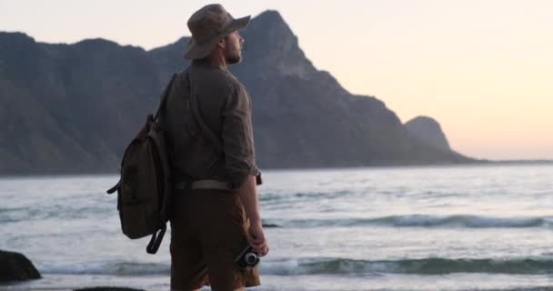Un viajero con una mochila se para en el océano, disfrutando del amor al atardecer salvaje — Vídeo de stock