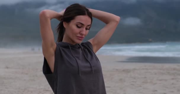 Dívka před tréninkem na pláži moře váže ocas a nasazuje si kapuci — Stock video