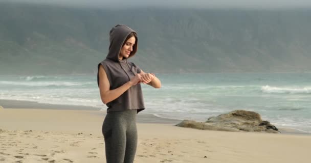 Junge Frau überprüft Fortschritte bei der Smart Watch. Sportlerin ruht sich am Strand aus — Stockvideo