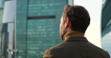 Adam gözlük takıyor ve gökdelendeki ofis binalarına bakıyor.