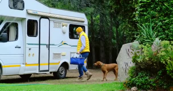 Un homme près du camping-car caresse deux chiens, l'herbe est arrosée — Video
