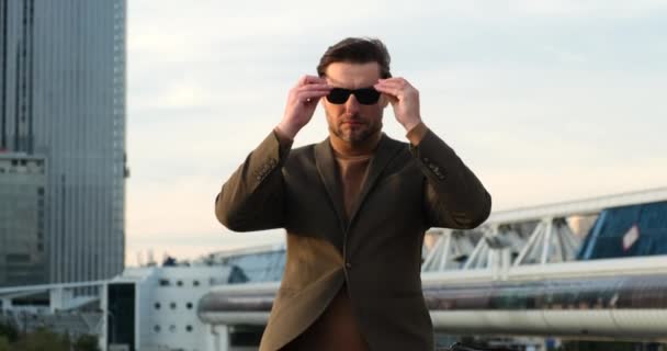 En man i kostym och solglasögon tittar på kameran med armarna i kors — Stockvideo