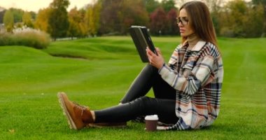 İş gözlüklü güzel genç bayan parkta tabletle ders çalışıyor..