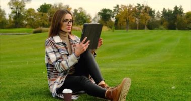 İş gözlüklü güzel genç bayan parkta tabletle ders çalışıyor..