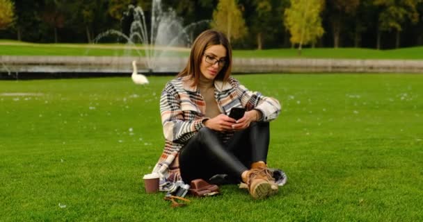 Bella giovane studentessa in occhiali da lavoro studio con telefono nel parco. — Video Stock