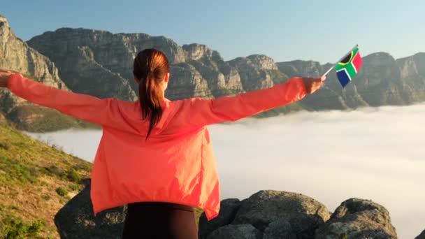 Dziewczyna stoi na szczycie góry w miasteczku peleryna z flagą Południowej Afryki — Wideo stockowe