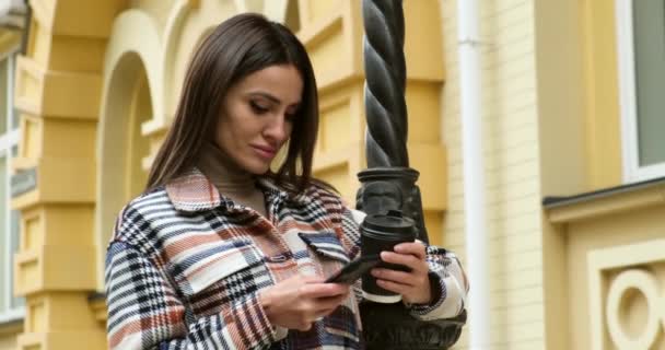 Νεαρή γυναίκα που στέκεται στο δρόμο πίνοντας τον καφέ να πάμε και χρήση κινητού τηλεφώνου — Αρχείο Βίντεο