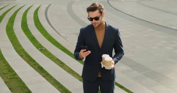 Uomo caucasico a piedi passi giù in strada, toccando smartphone e bere — Video Stock