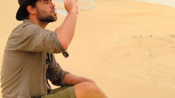 Człowiek czuje pragnienie i pije wodę na pustyni. samotny podróżnik siedzi na piasku — Wideo stockowe