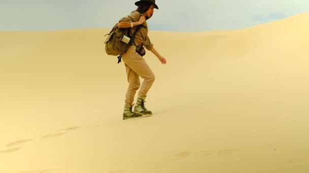 Traveler girl with a backpack on her back and trekking boots walks on the sand — Stockvideo