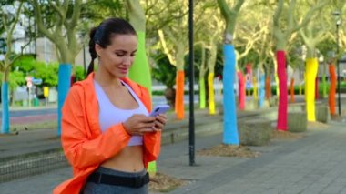 Gülümseyen sporcu kız sokakta duruyor ve erkek arkadaşına bir mesaj yazıyor.